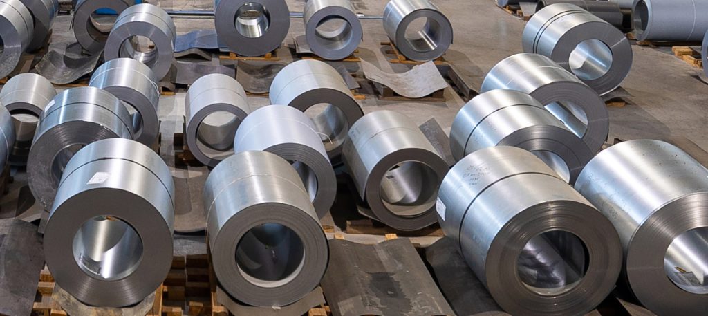 En la imagen podemos observar una gran cantidad de bobinas de acero inoxidable, dispuestas a lo largo del suelo de una nave industrial
