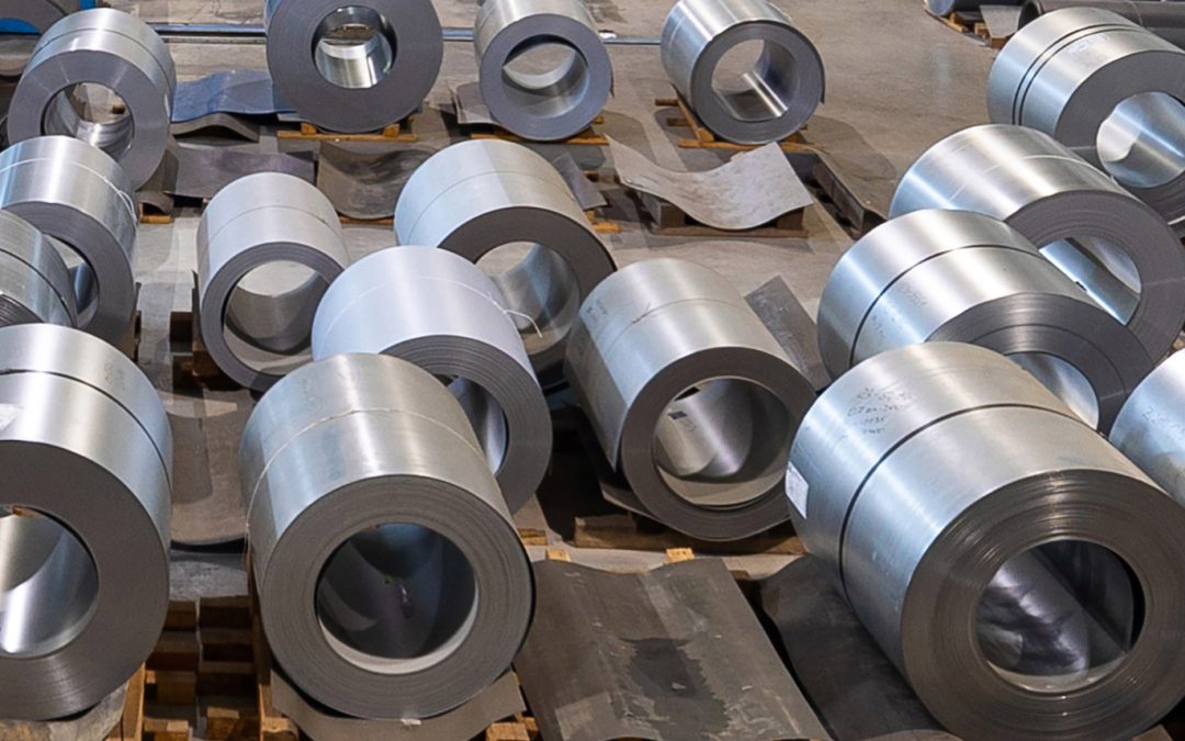 En la imagen podemos observar una gran cantidad de bobinas de acero inoxidable, dispuestas a lo largo del suelo de una nave industrial